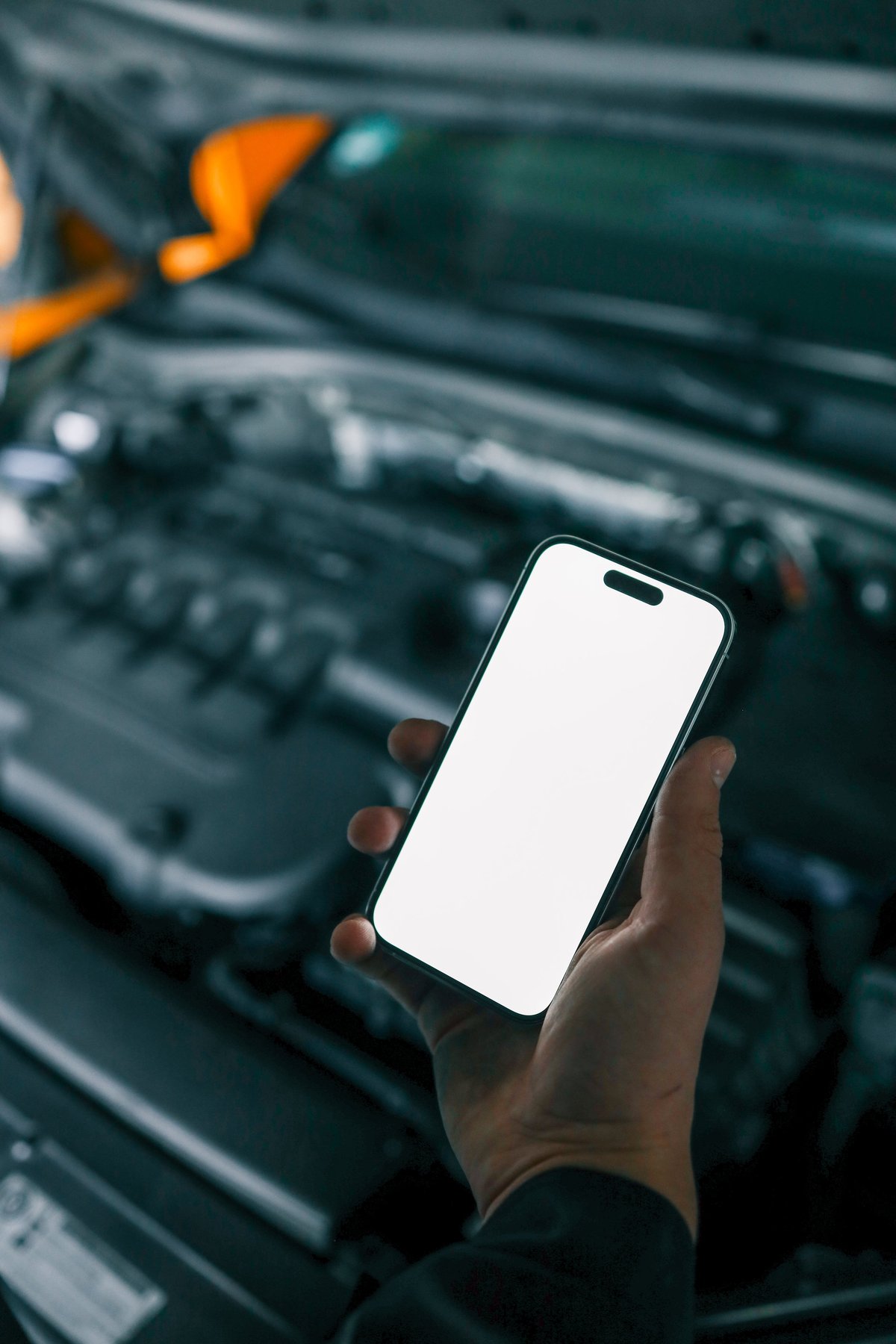 Mechanic holding smartphone with open car engine